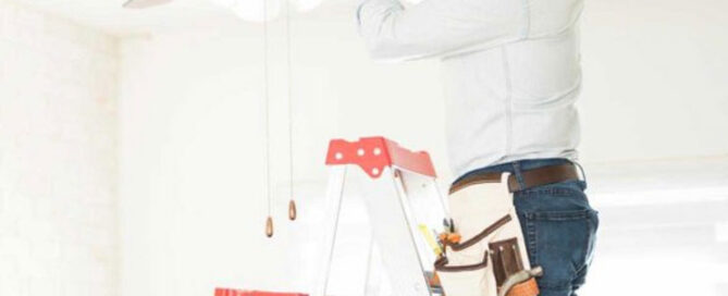 Prescott electrician installing a ceiling fan from a ladder in a living room