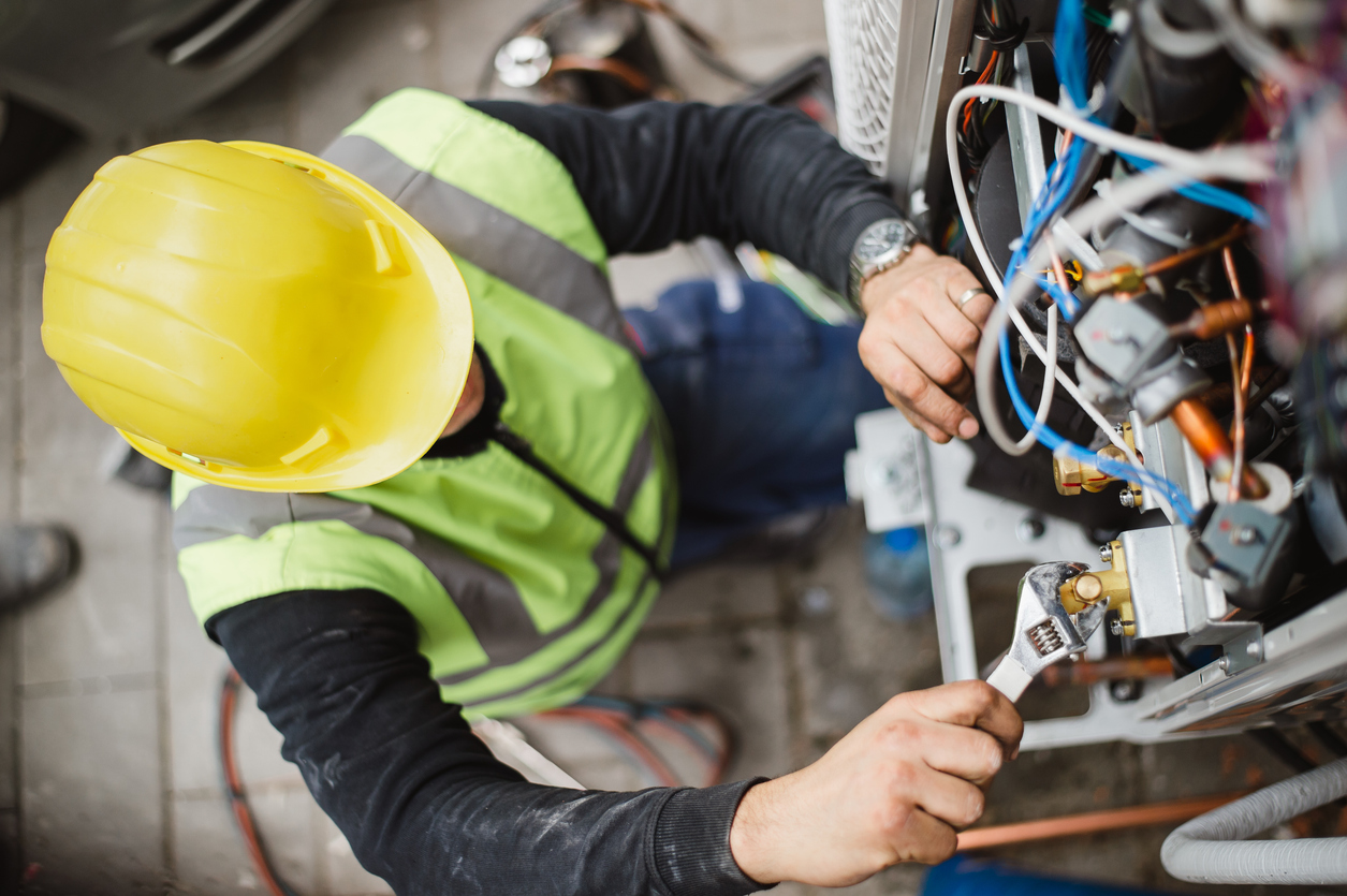 AES Commercial electrician installing a wall outlet with a drill, inspecting wires during a building renovation.