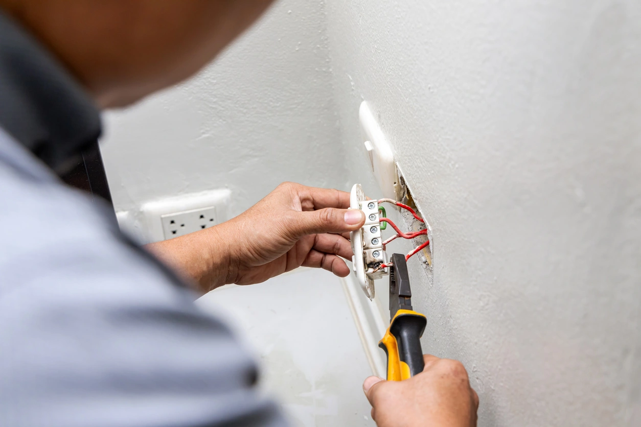 Electrician in Wilhoit AZ repairing wall outlet wiring with pliers