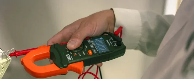 An electrician checks a wall outlet with a clamp meter, showing electrical safety tips for Prescott homes