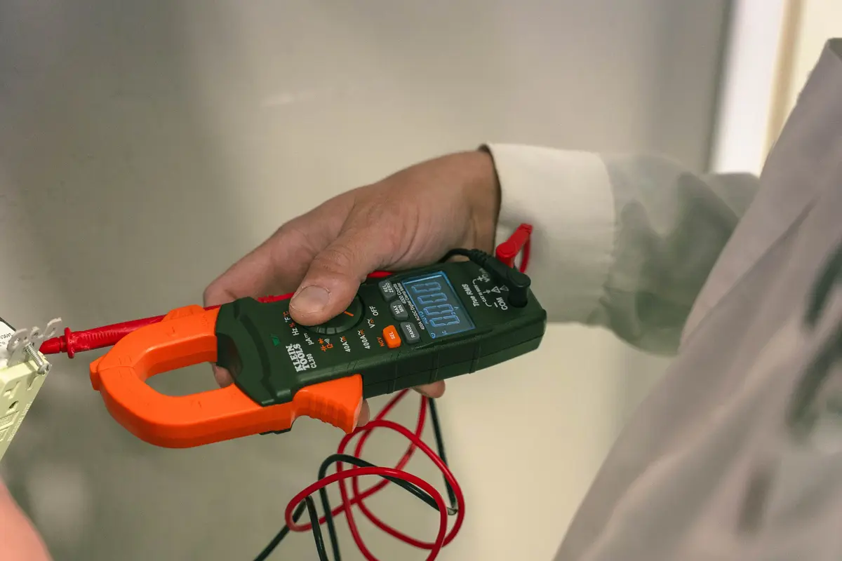 An electrician checks a wall outlet with a clamp meter, showing electrical safety tips for Prescott homes