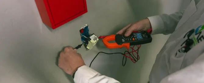 Electrician tests wall wiring with meter, showing signs you need electrical rewiring in Prescott