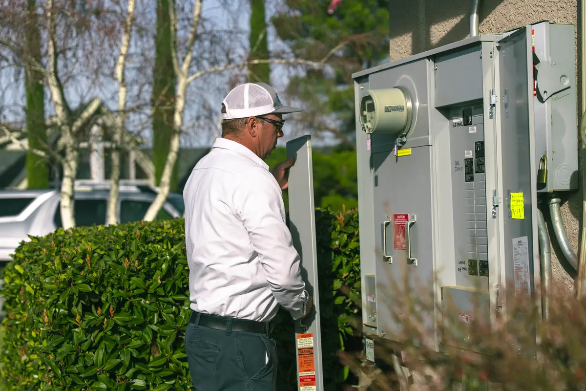 Electrical panel capacity guide shown through an electrician inspecting an outdoor residential electrical service panel.